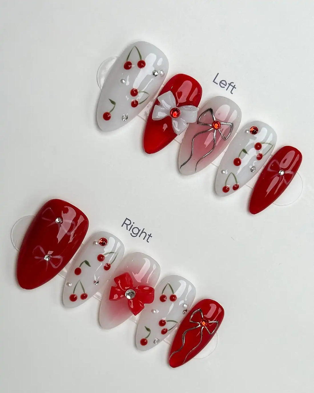 Handmade red and white press-on nails with cherry fruit, bow, and ribbon charm designs.