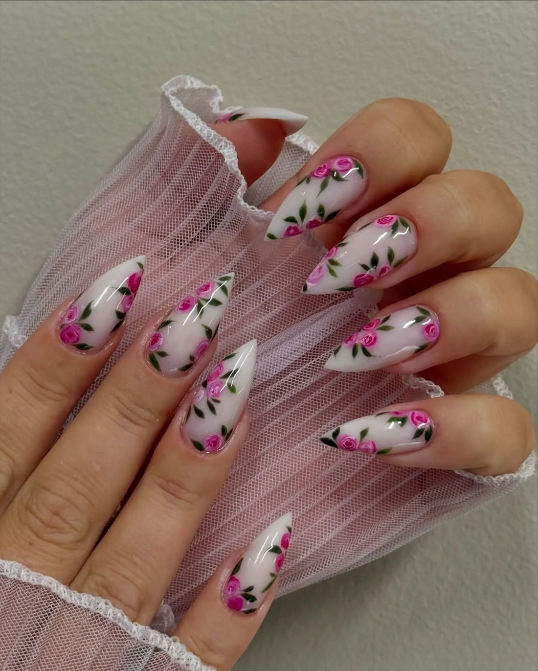Hand with long stiletto press-on nails featuring hot pink rose floral design