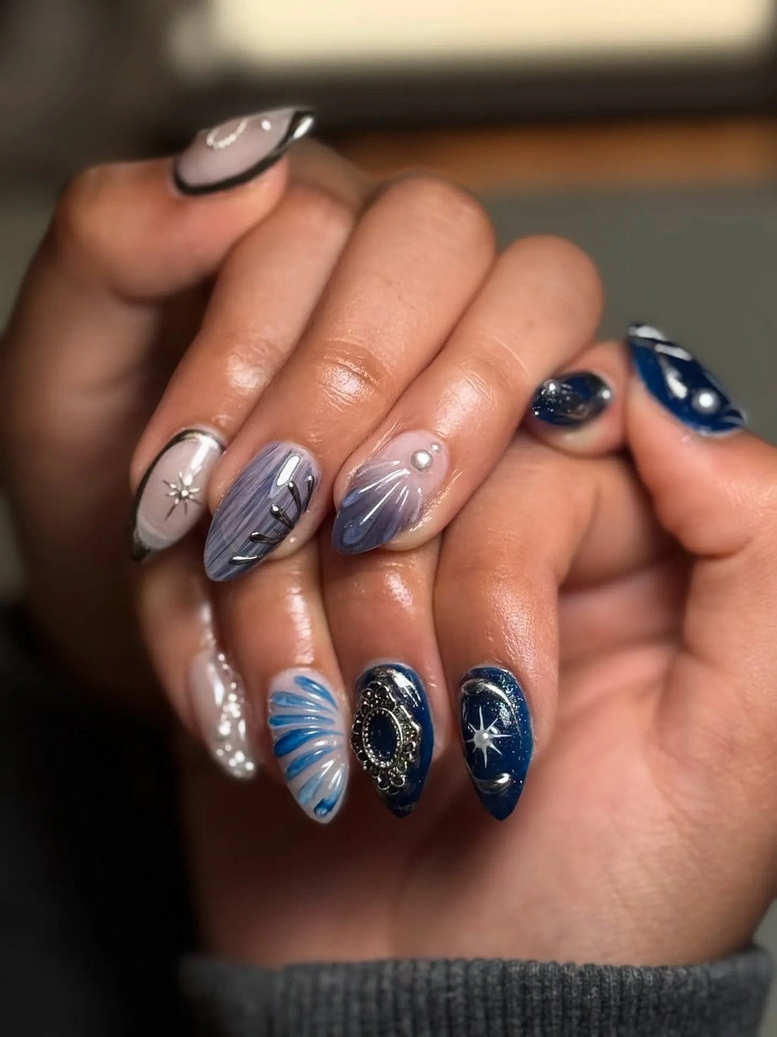 Hand with royal blue shimmer press-on nails featuring 3D pearl charms and starburst designs.