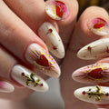 Handmade press-on nails with red heart and gold fleur-de-lis designs, adorned with gems.