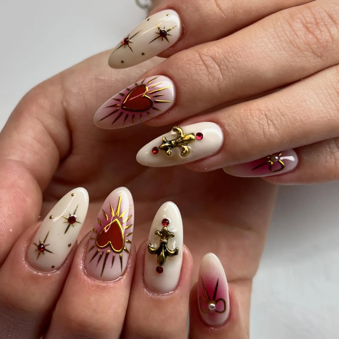 Handmade press-on nails with gold fleur-de-lis, red hearts, and gemstone accents
