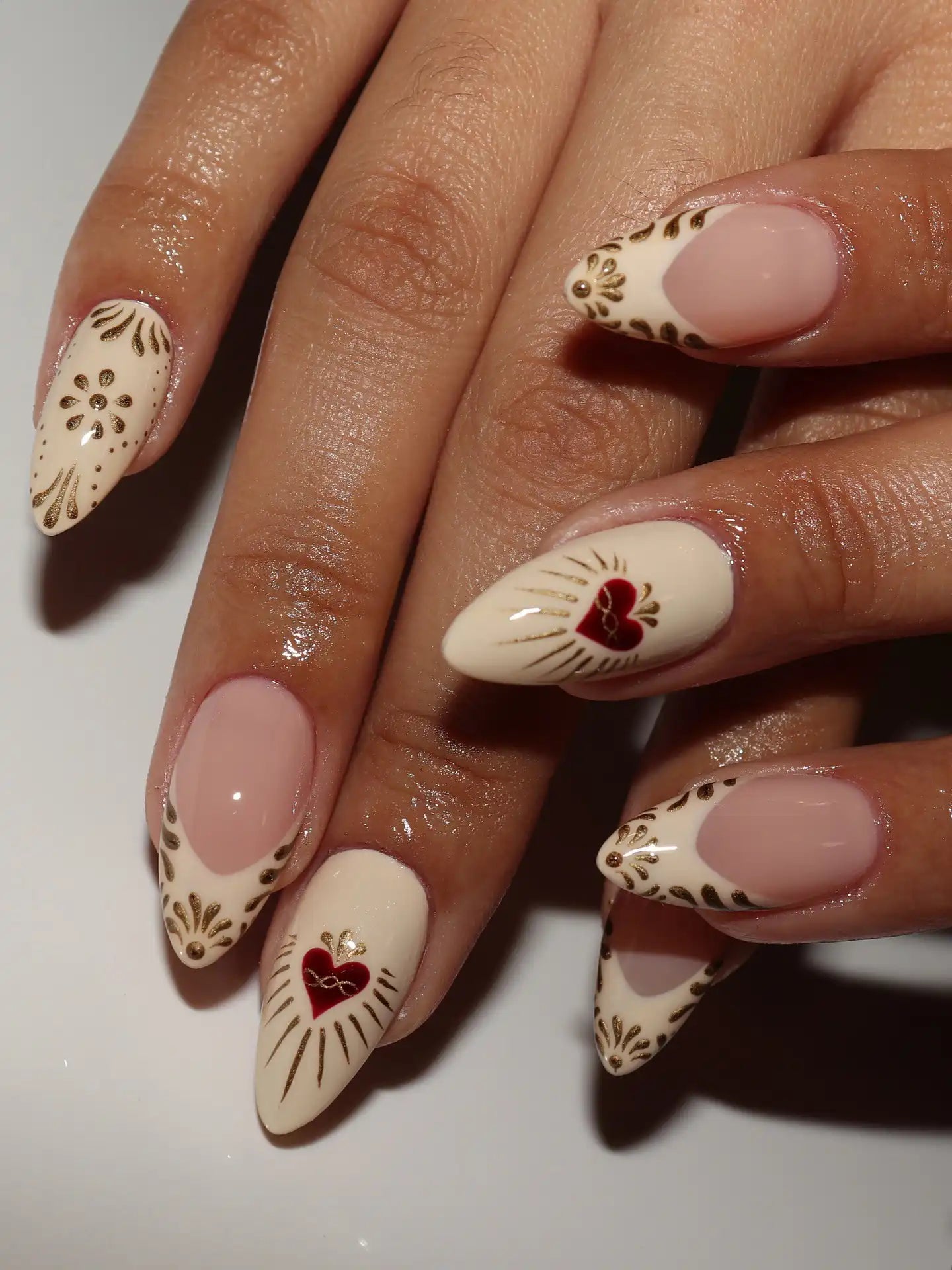 Handmade press-on nails with gold ornate patterns and red sacred heart accents on nude base