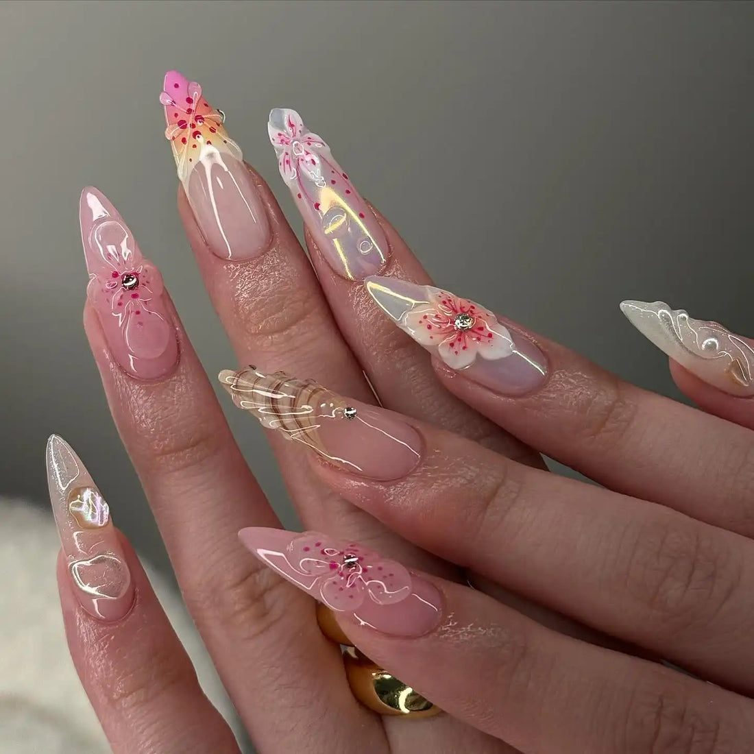 Hand with long, handmade press-on nails featuring 3D seashell and blossom flower designs.