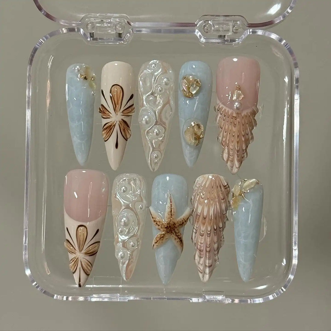 Handmade seashell and starfish press-on nails with ocean-themed 3D designs in blue and nude tones.