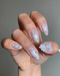 Hand with iridescent pearl 3D floral press-on nails featuring shimmering accents.