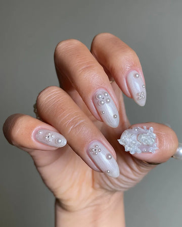 Hand with iridescent pearl 3D floral press-on nails featuring shimmering accents.