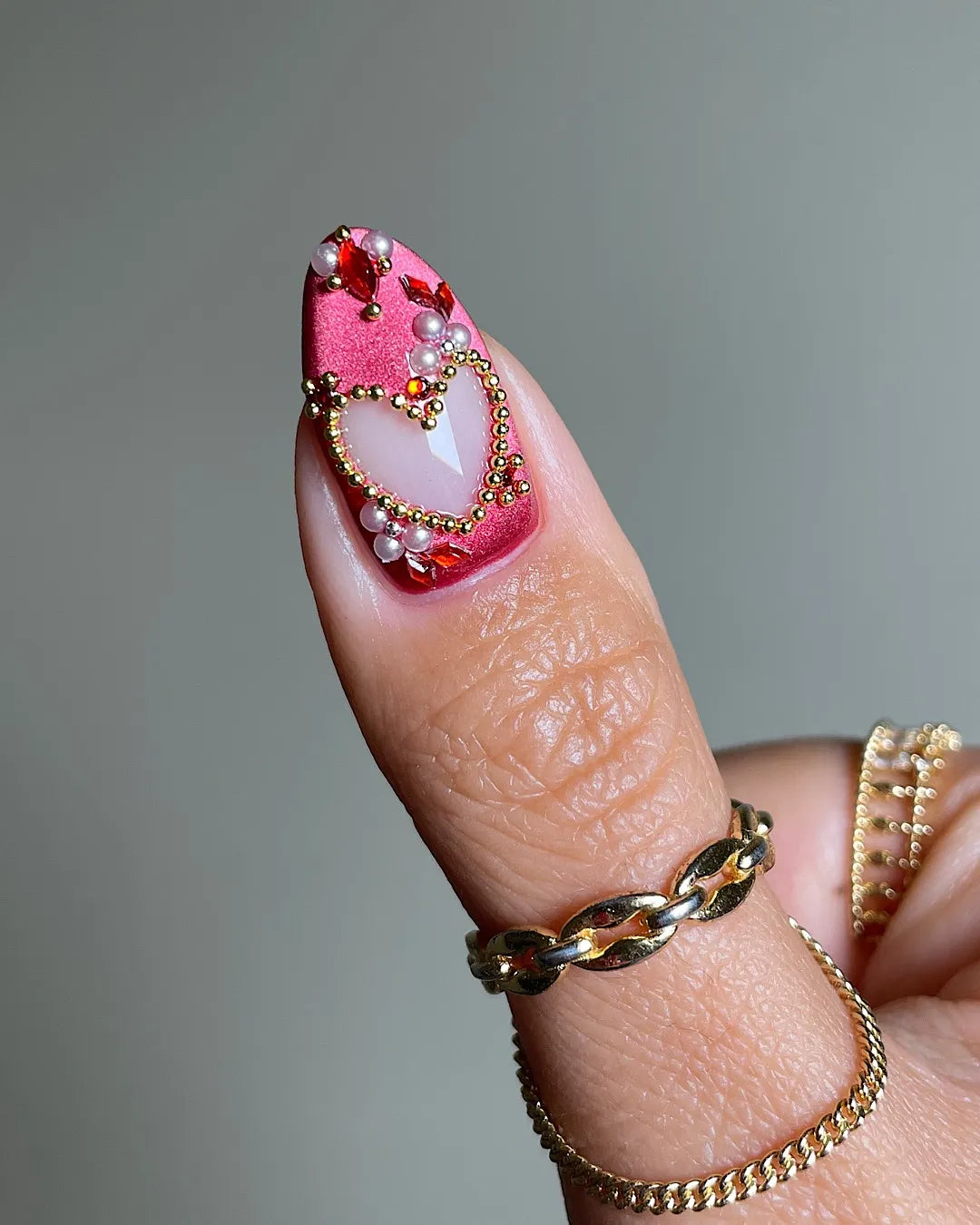Hand wearing shimmering red and burgundy press-on nails with gemstone and gold embellishments