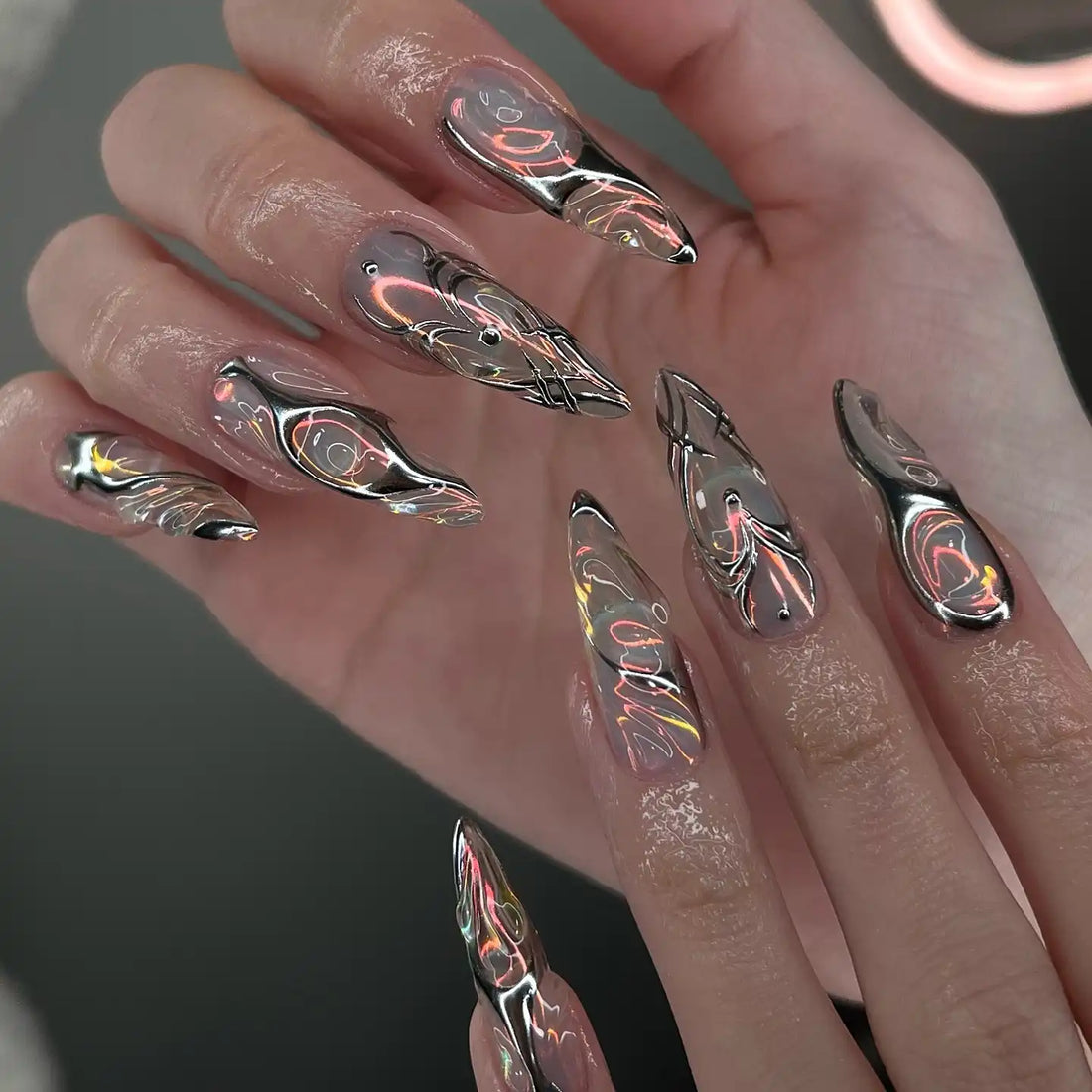 Hand with long chrome mirror press-on nails featuring handmade silver heart and abstract designs.