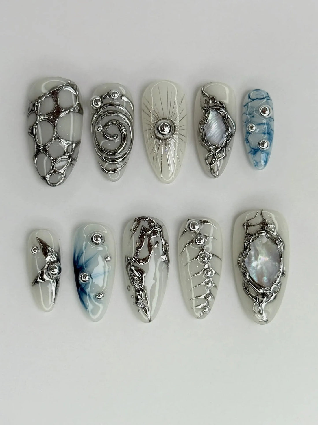 Handmade silver metallic chrome press-on nails with abstract and marble designs on white base.