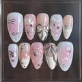 Handmade pink and white press-on nails with silver ribbon, bows, and gemstone accents