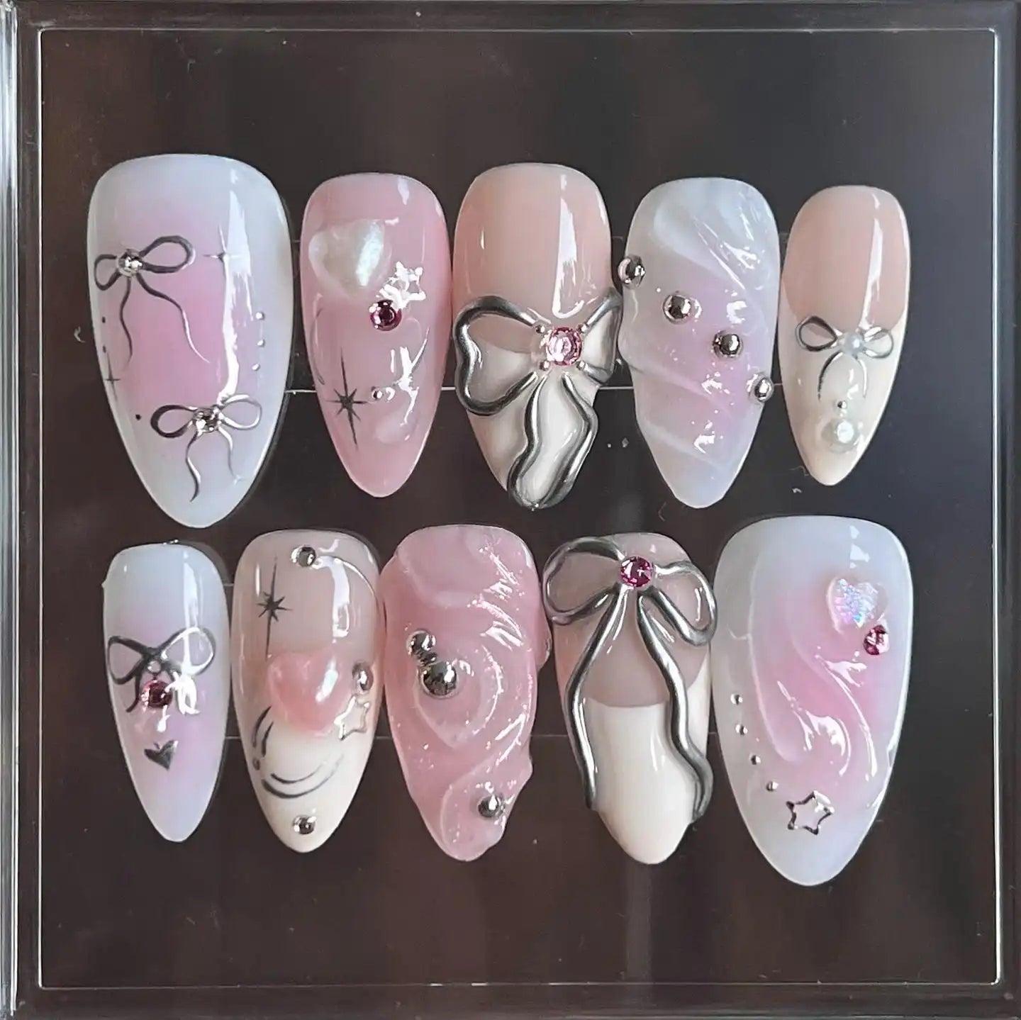 Handmade pink and white press-on nails with silver ribbon, bows, and gemstone accents
