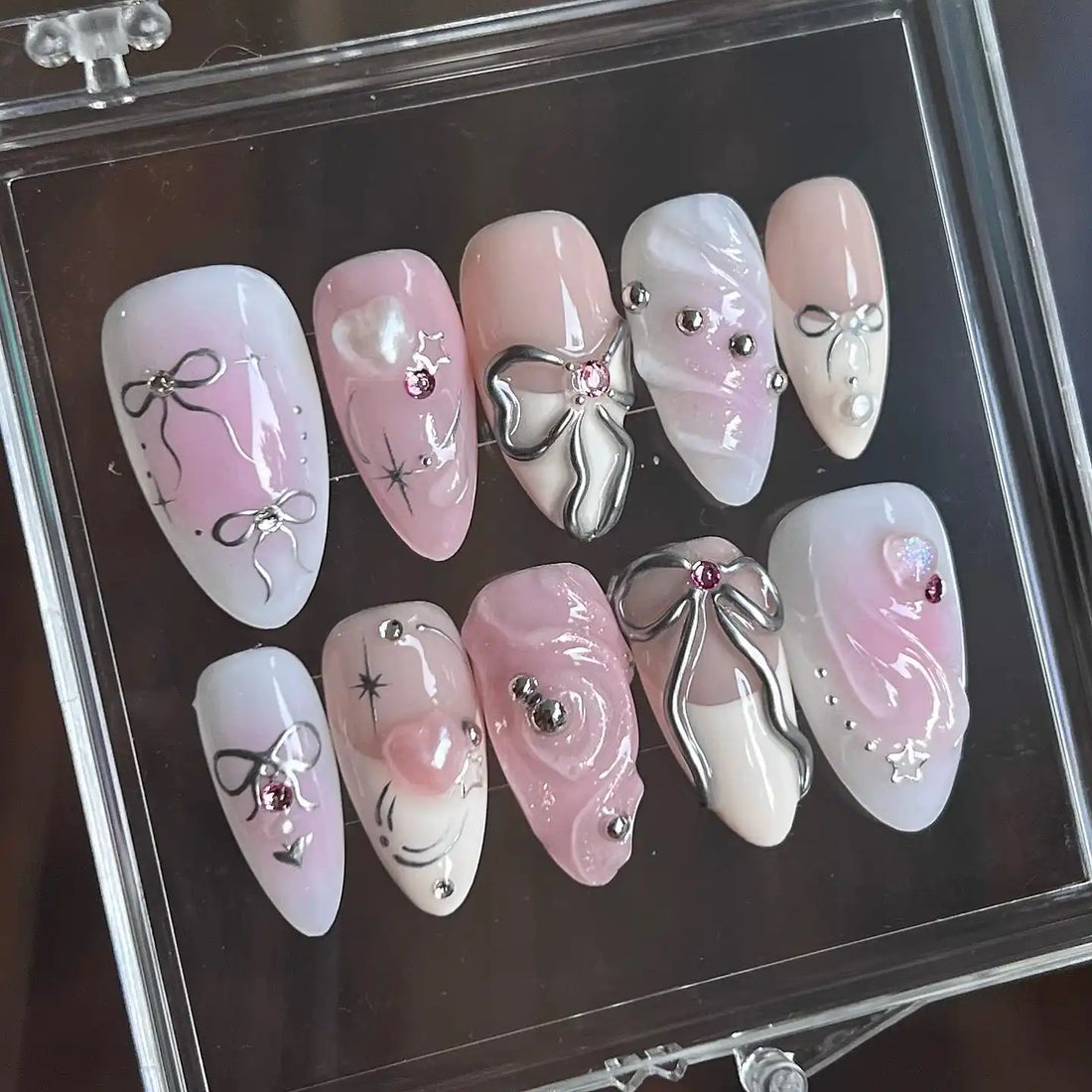 Handmade pink and white press-on nails with silver ribbon, bows, and gemstone accents