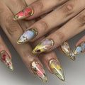 Handmade press-on nails with gold leaf edging and spring floral designs in pastel colors.