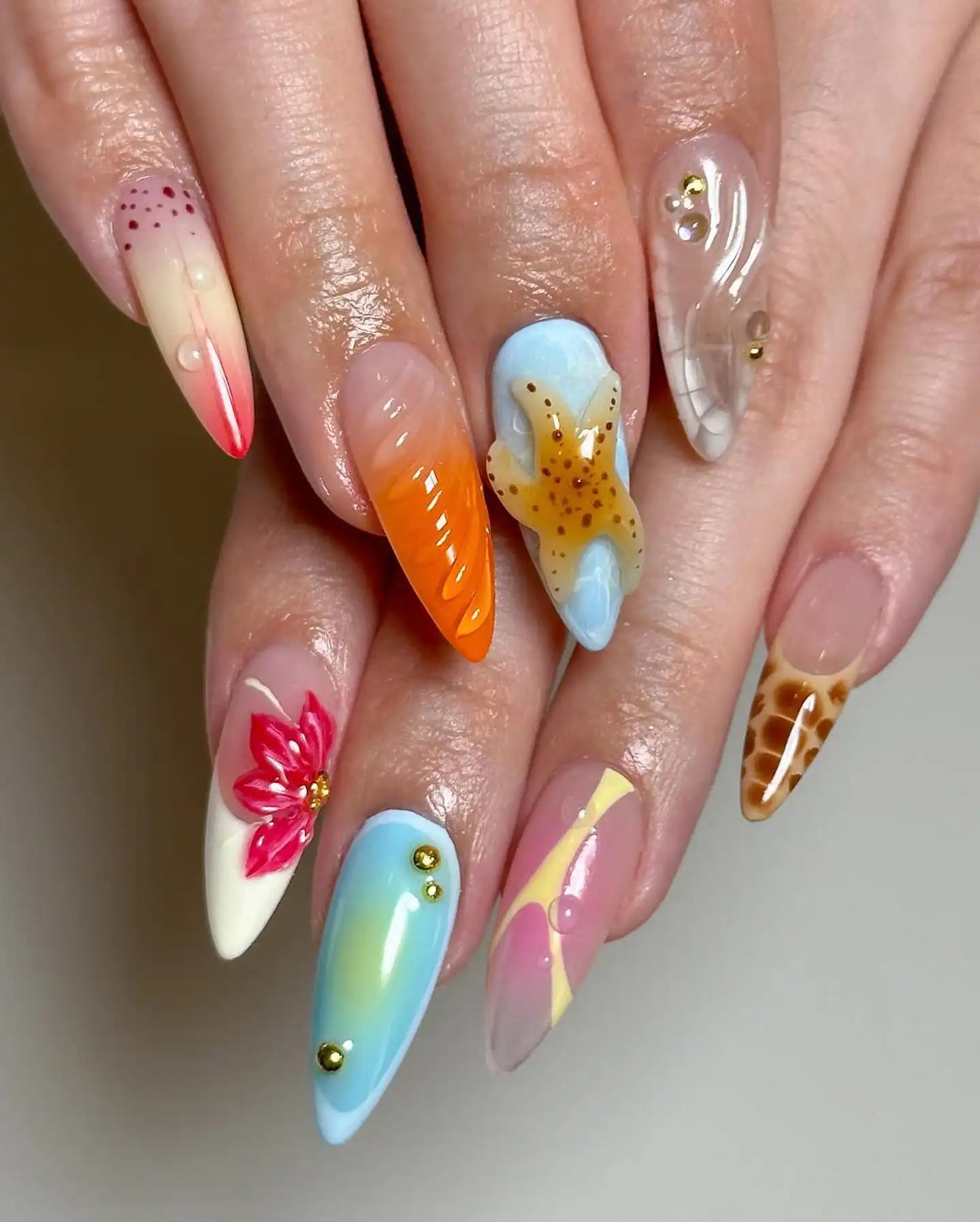 Hand with long, handmade summer press-on nails featuring starfish, floral, and snake skin designs.