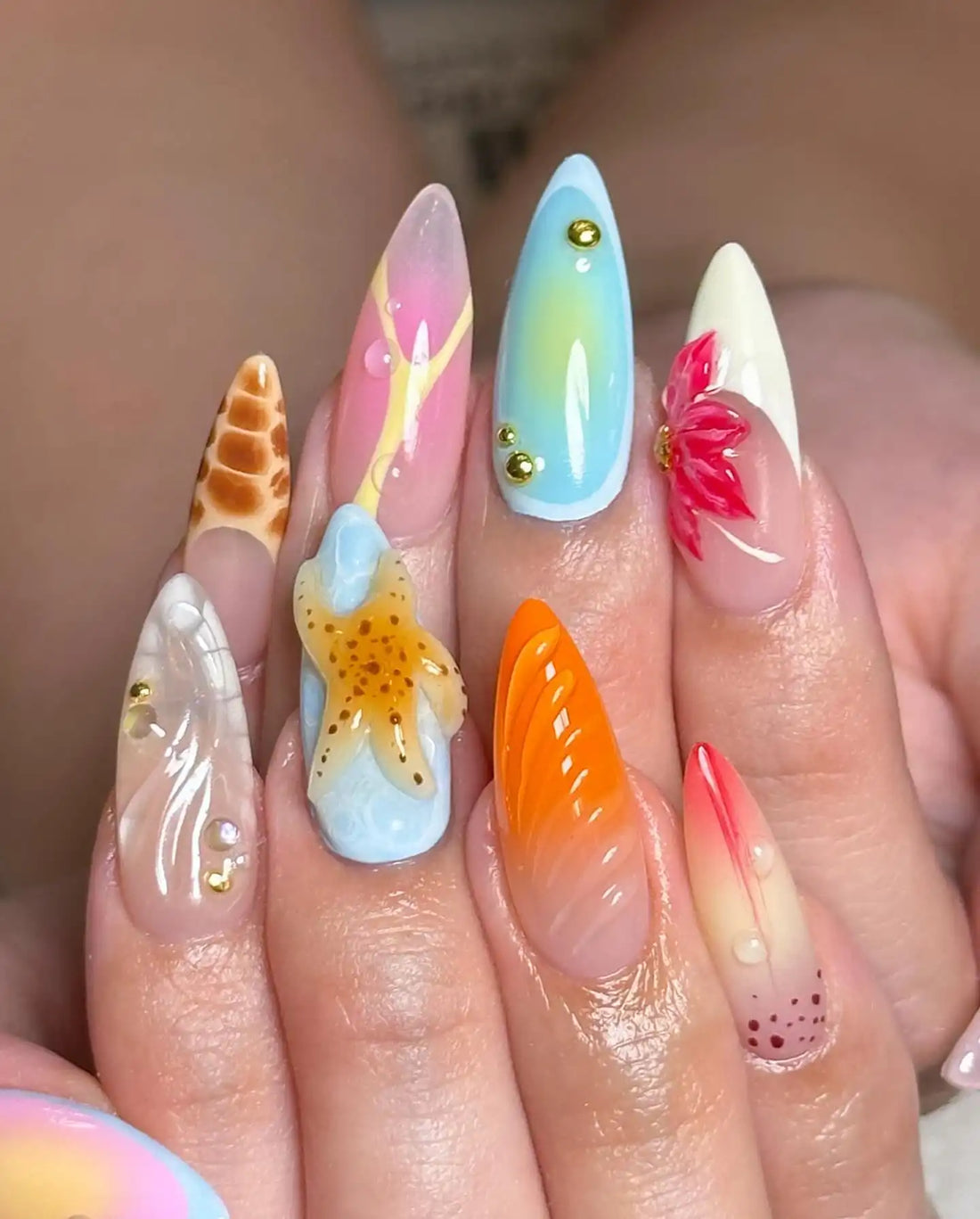 Hand with long, handmade summer press-on nails featuring starfish, floral, and snake skin designs.