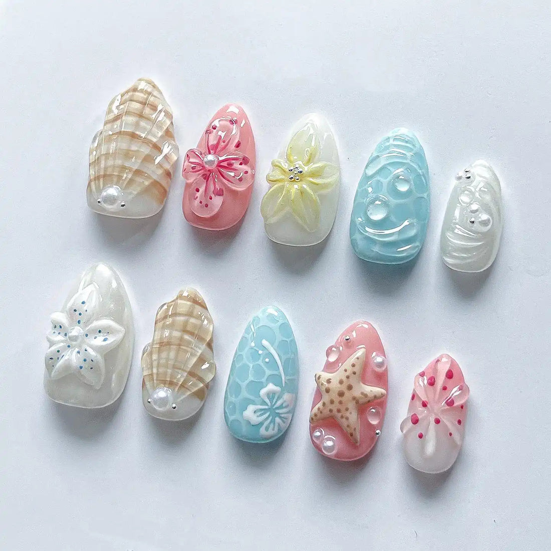 Handmade pastel beach press-on nails with starfish, seashell, and floral designs on white background.