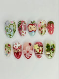 Handmade press-on nails with strawberry, apple, gingham, and floral designs, colorful gems