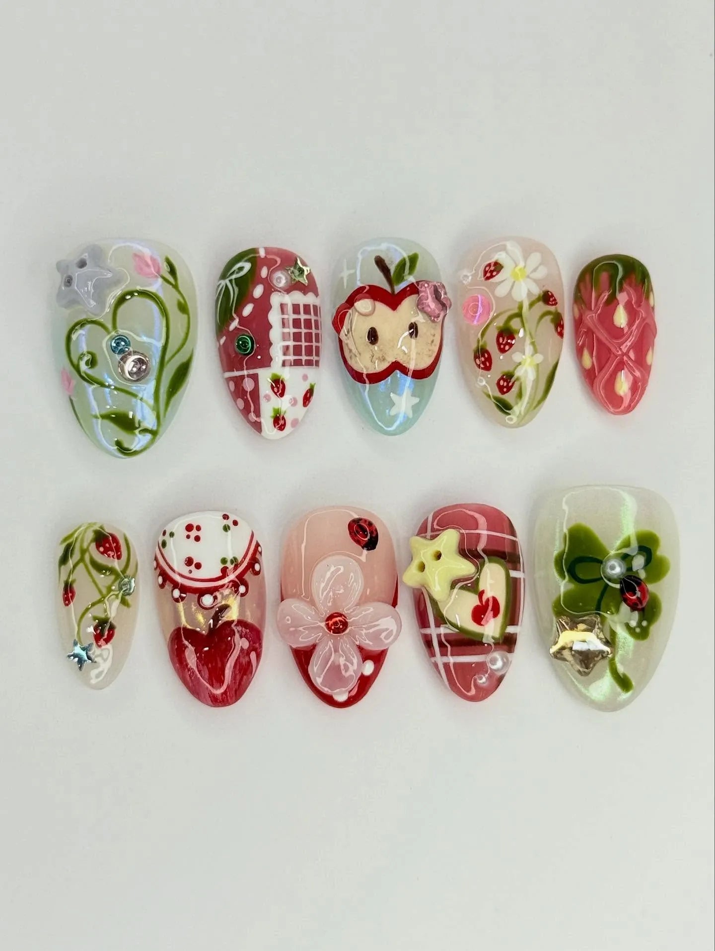 Handmade press-on nails with strawberry, apple, gingham, and floral designs, colorful gems