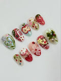 Handmade press-on nails with strawberry, red apple, gingham, and floral designs on a white background.
