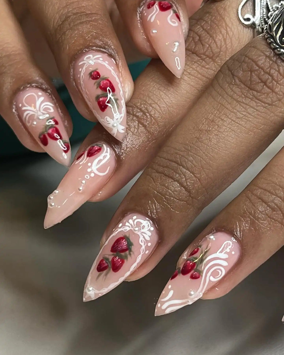 Handmade press-on nails with strawberry designs and white swirl accents on almond-shaped tips