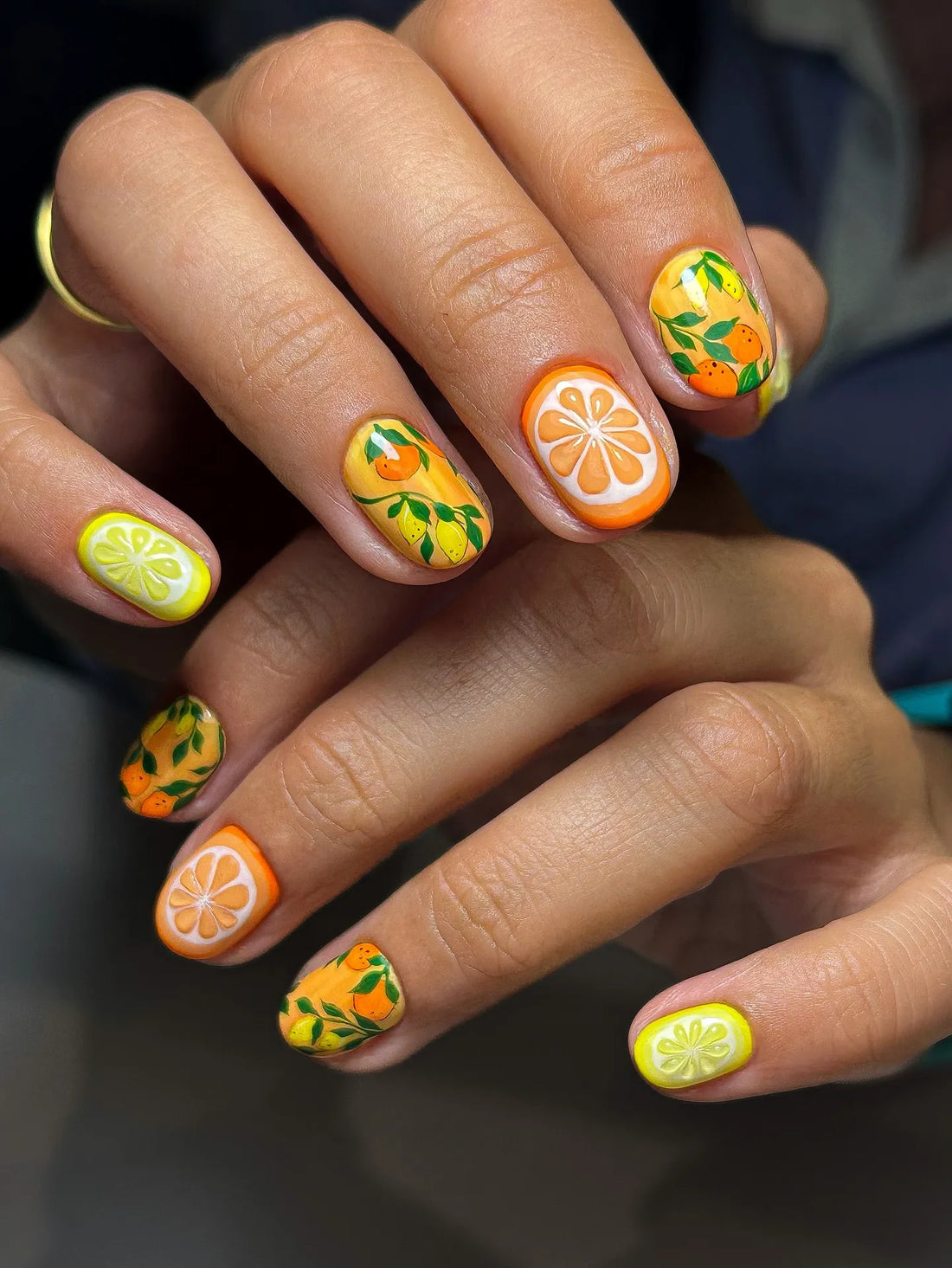 Hand with handmade press-on nails featuring citrus lemon and orange fruit garden art design.