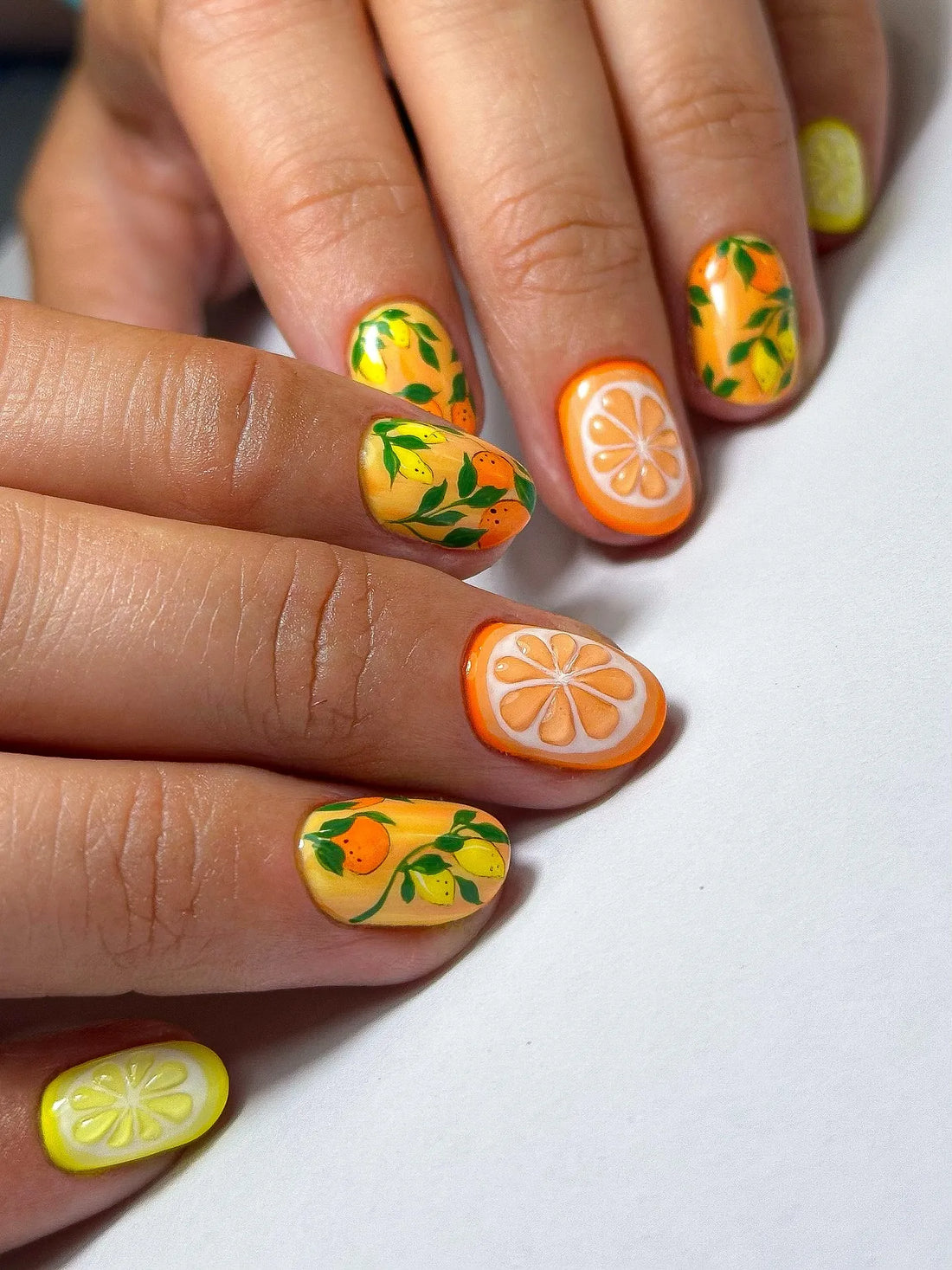 Hand with handmade press-on nails featuring citrus lemon and orange fruit garden art design.