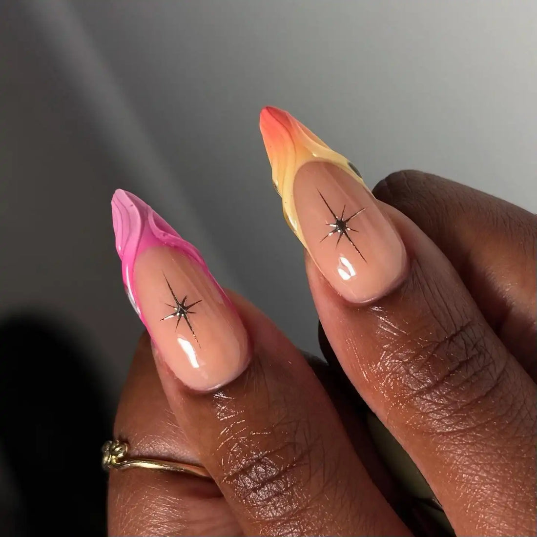 Hand with long press-on nails, featuring colorful gradient, shell, and summer-inspired designs.