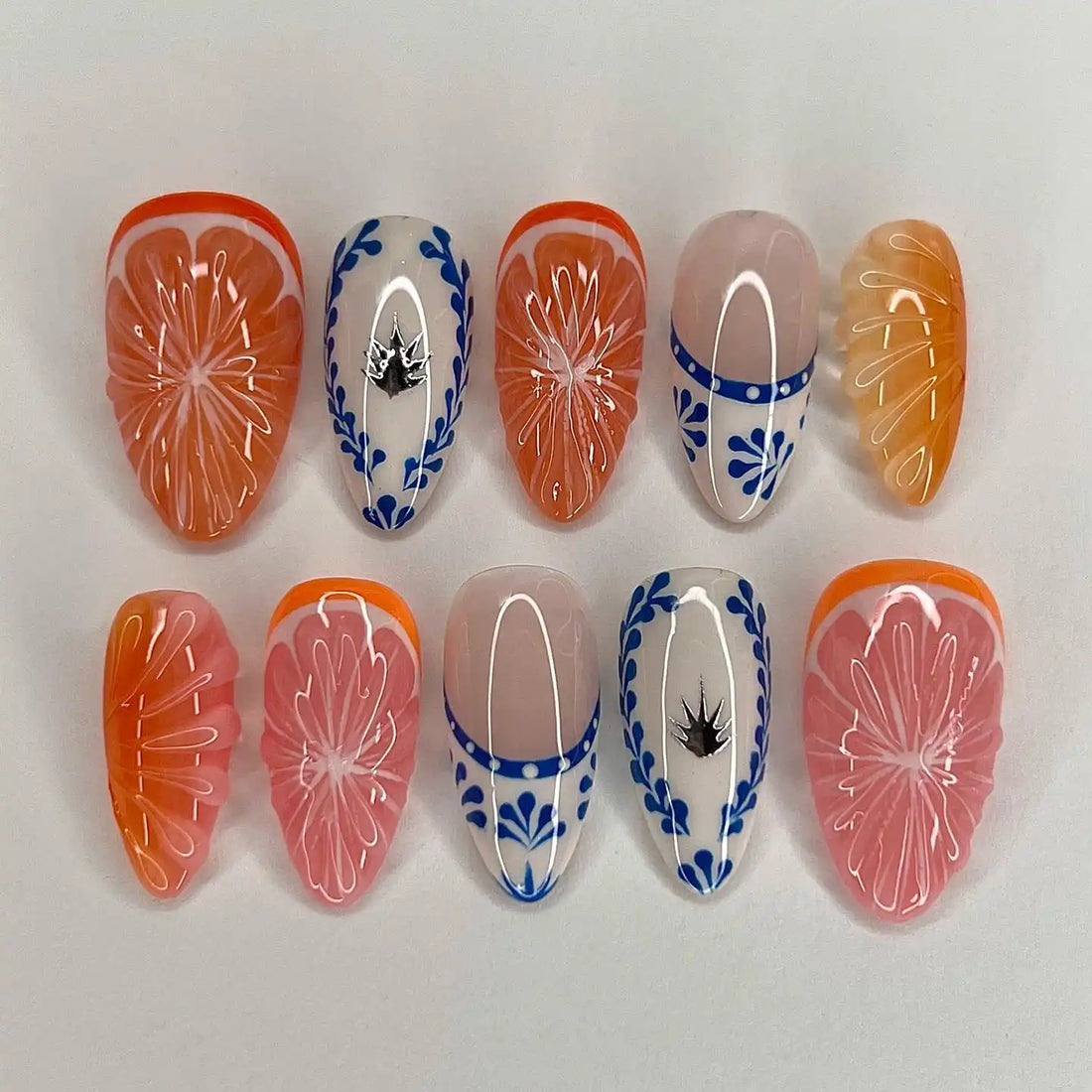 Handmade press-on nails with orange and pink fruit designs, blue floral accents, and glossy finish.