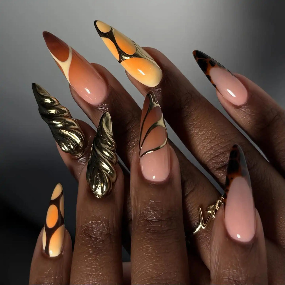 Hand with long press-on nails in summer orange gradient and metallic gold accent designs.