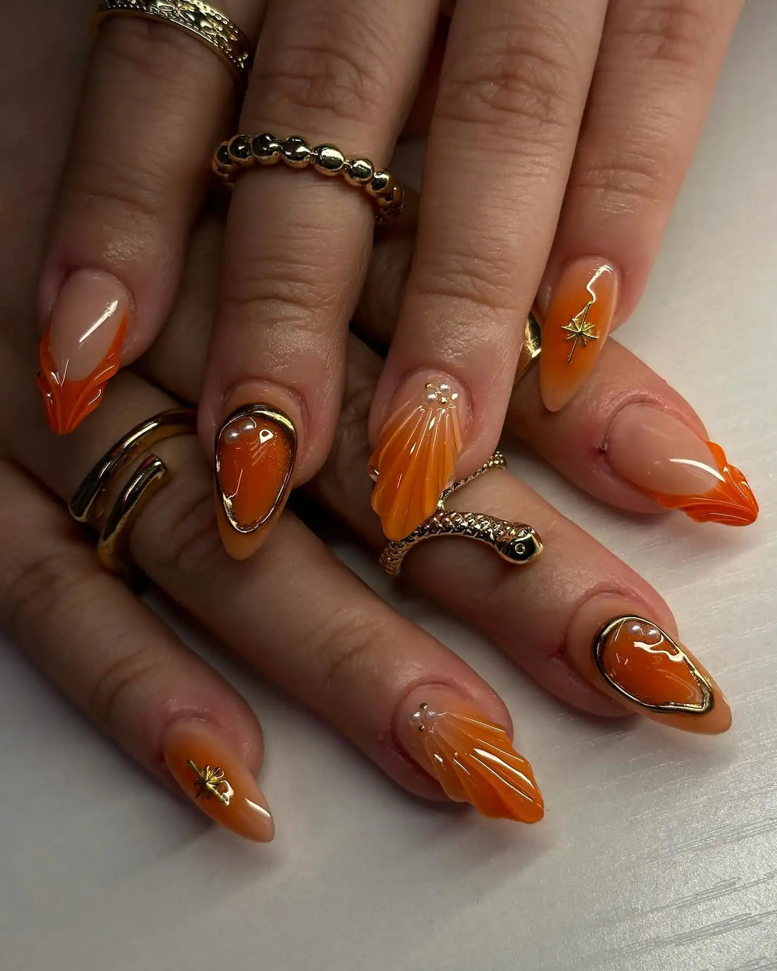 Handmade press-on nails with orange shell design and gold accents on manicured hands