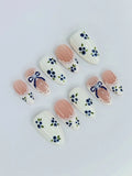 Handmade press-on nails with blue floral, gingham, lace, and ribbon bow designs on white and nude.
