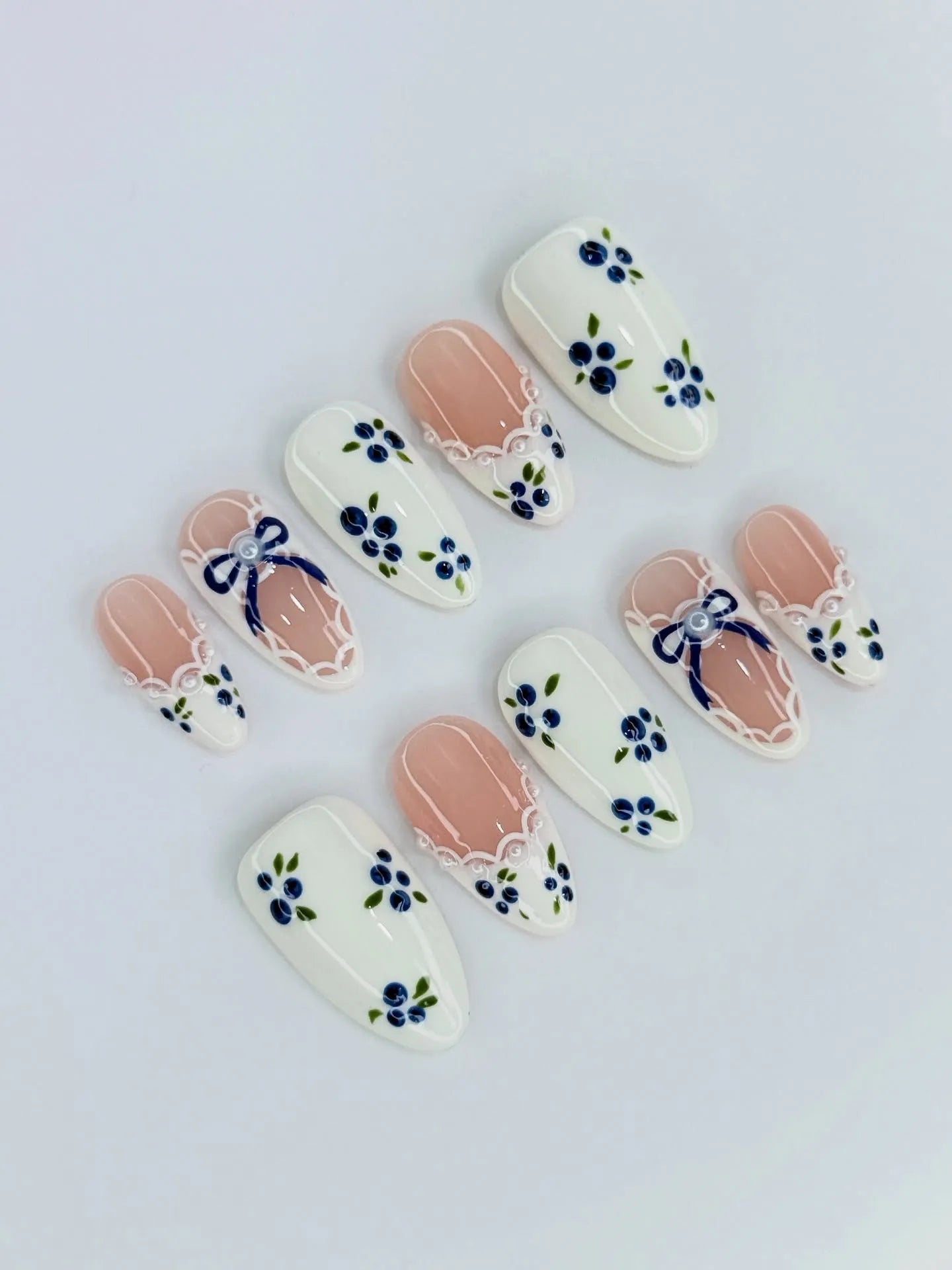 Handmade press-on nails with blue floral, gingham, lace, and ribbon bow designs on white and nude.