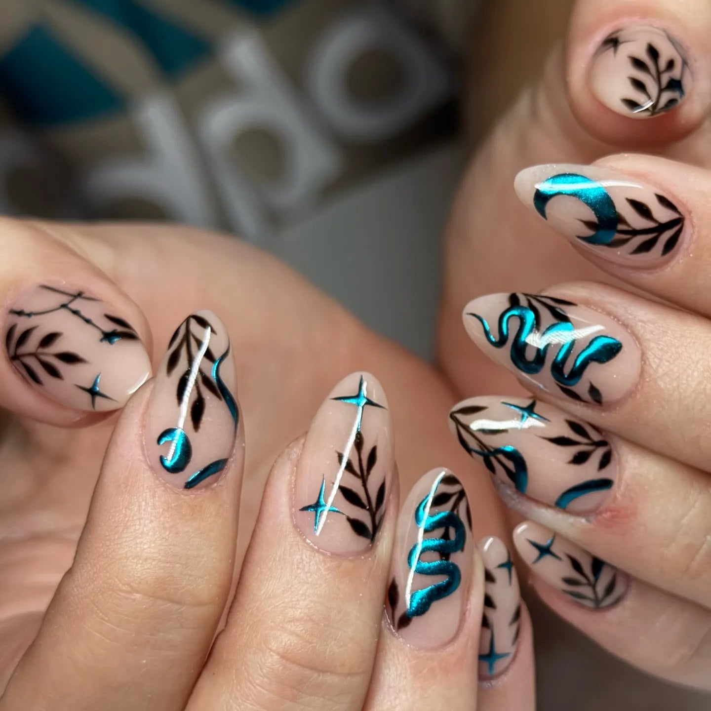 Handmade press-on nails with teal chrome snake, moon, stars, and black leaf designs.