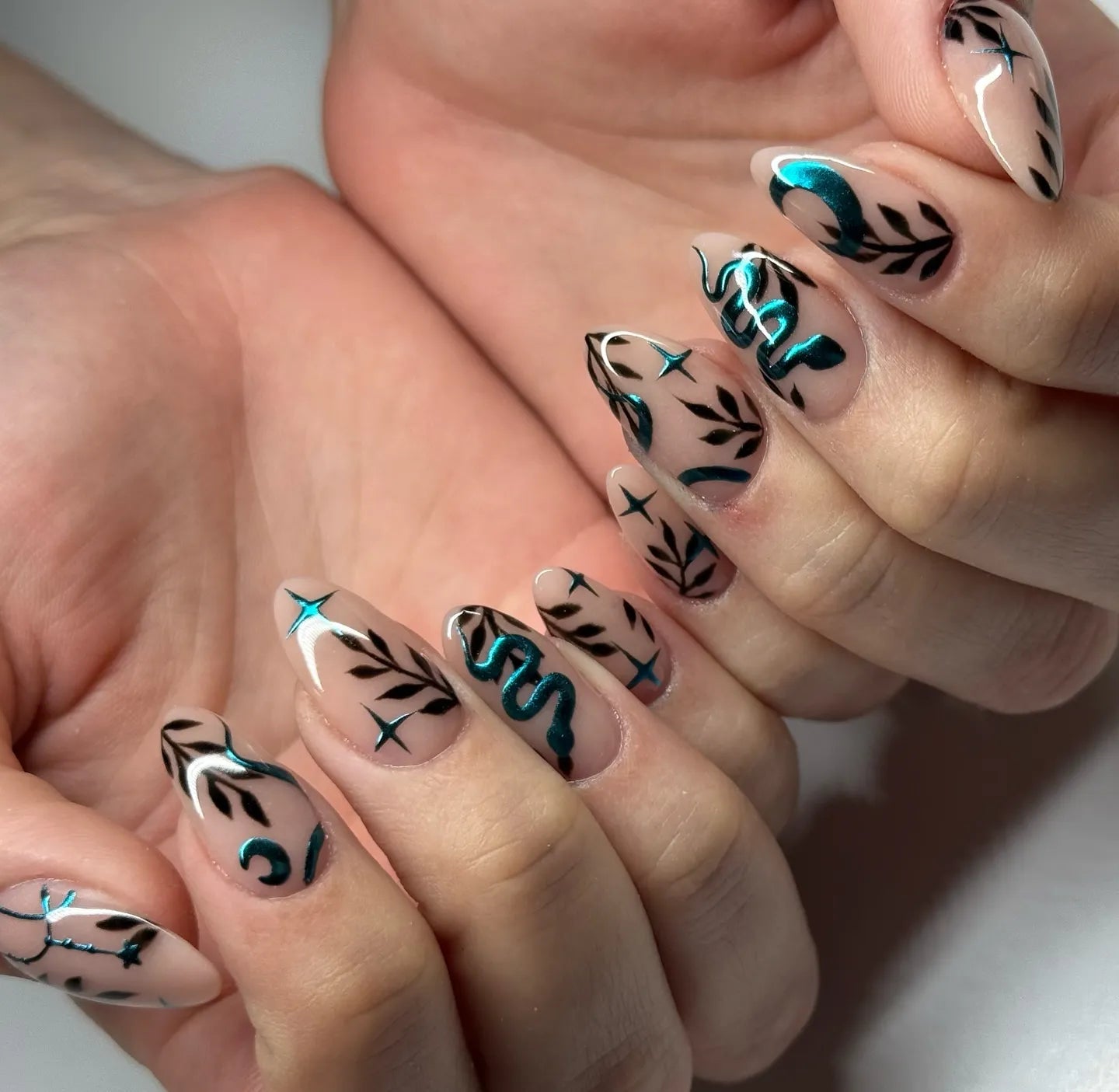 Handmade press-on nails with teal chrome snake, moon, stars, and black leafy designs