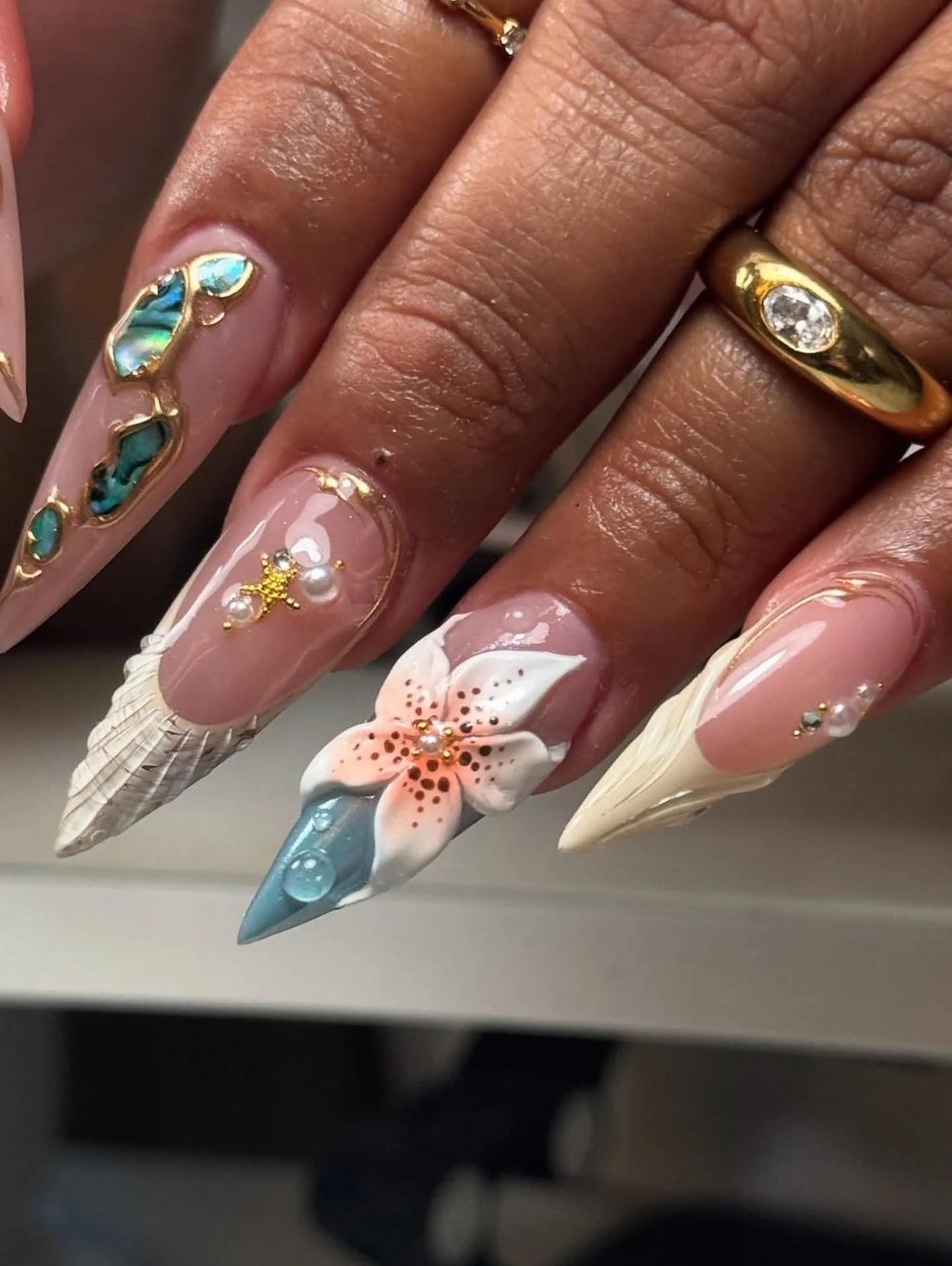 Hand with long handmade press-on nails featuring teal, abalone, flower, and shell designs.