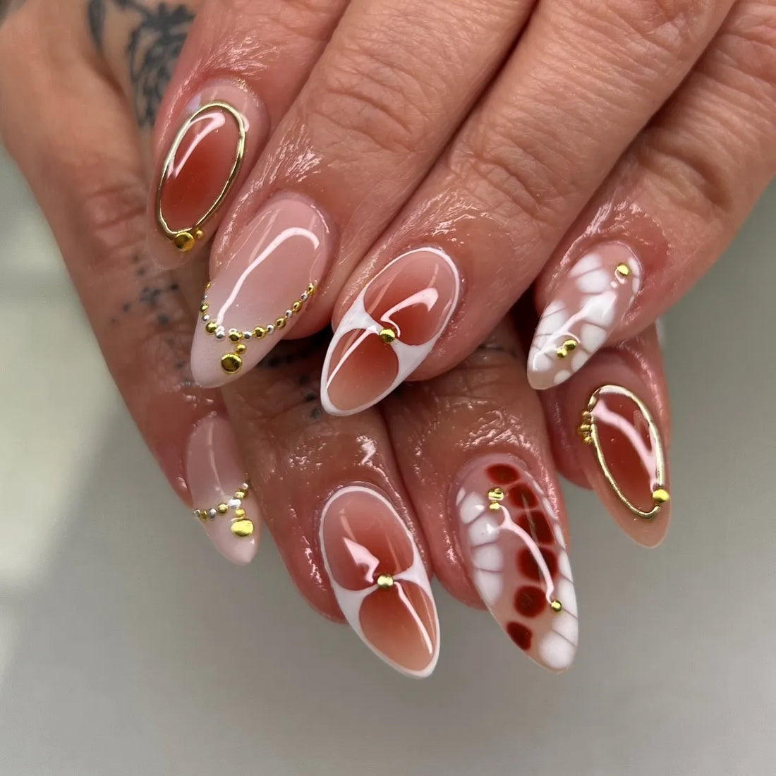 Hand with bohemian abstract press-on nails in terracotta, white, and gold accents