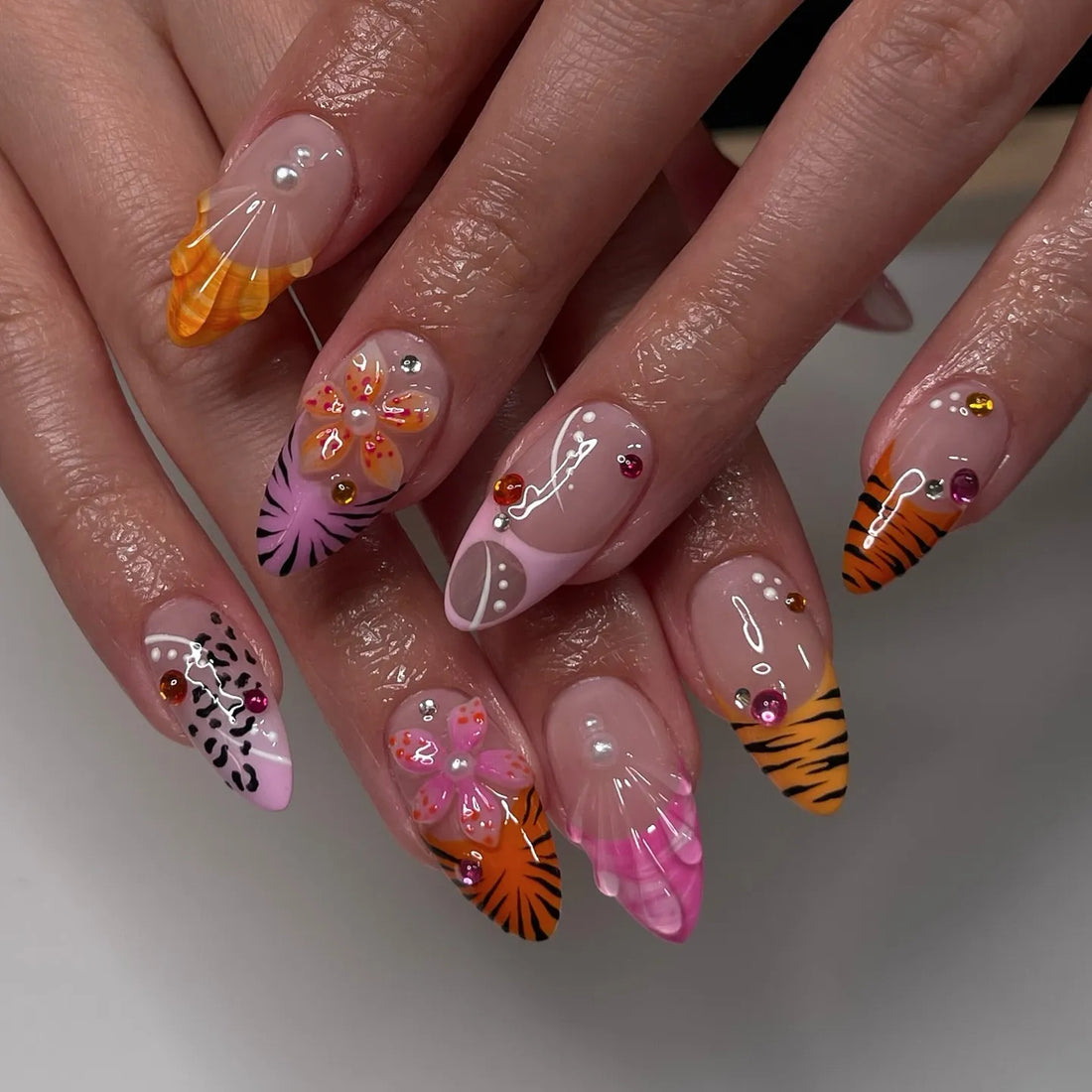 Handmade press-on nails with tiger stripes, pink and orange floral designs, and bead accents