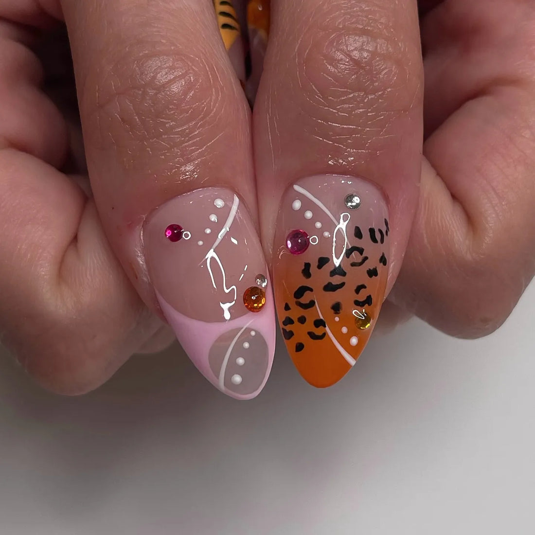 Handmade press-on nails with tiger stripes, pink and orange floral designs, and bead accents