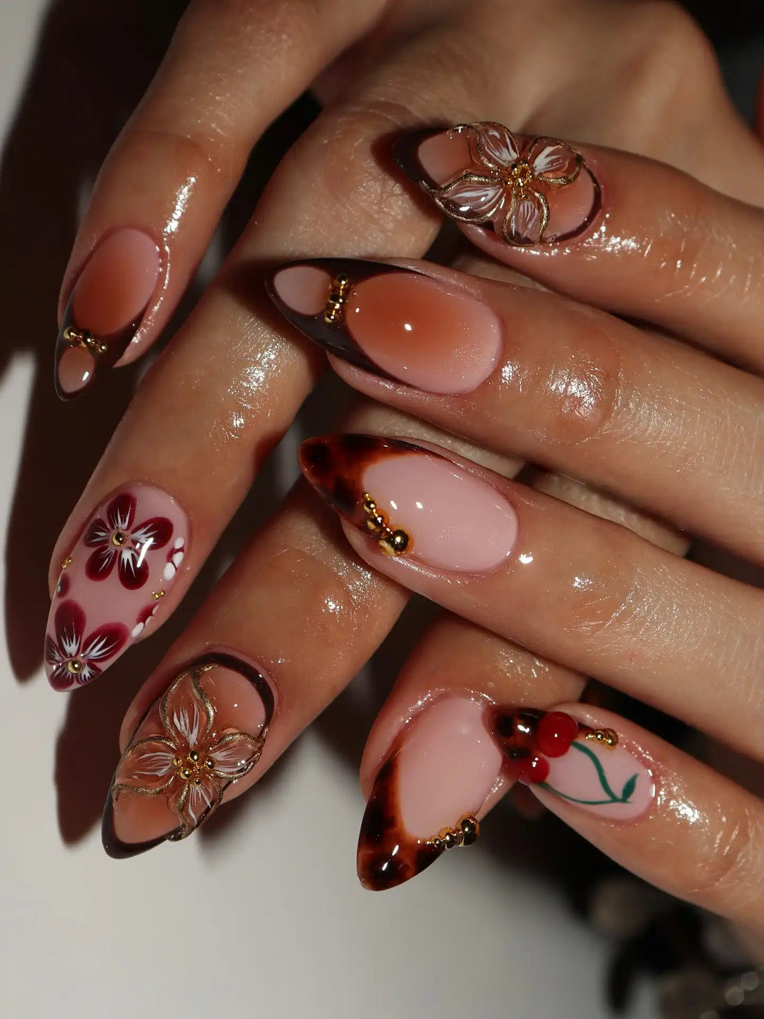 Hand with almond-shaped handmade tortoise shell ombré press-on nails featuring autumn floral designs and gold accents.
