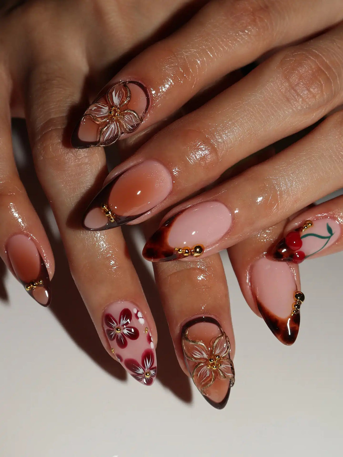 Hand with almond-shaped handmade tortoise shell ombré press-on nails featuring autumn floral designs and gold accents.
