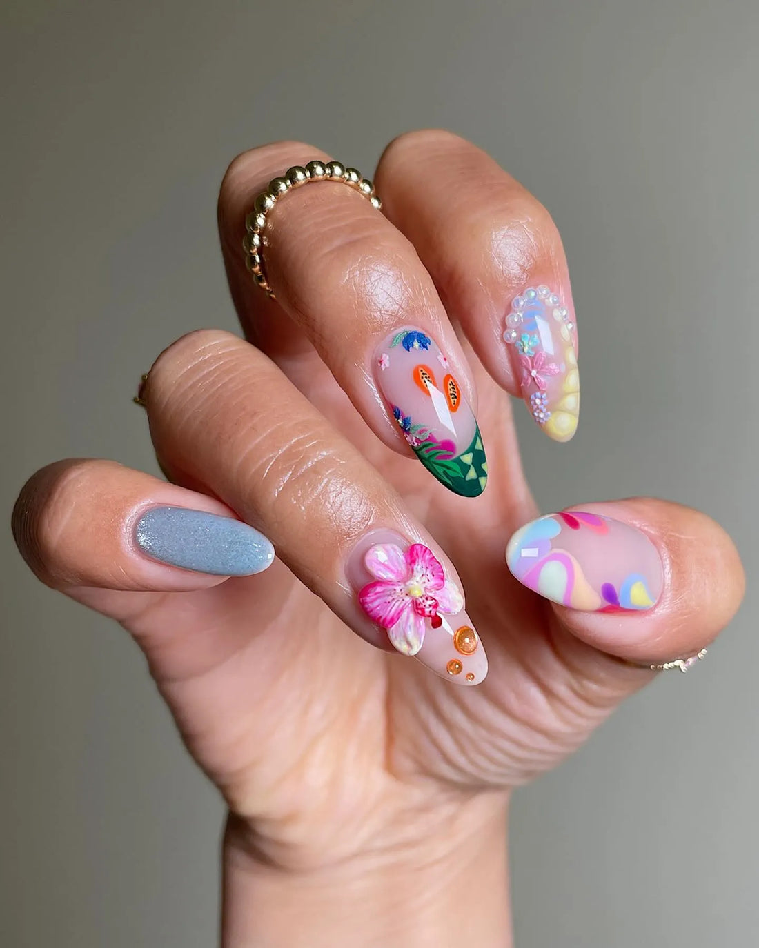 Hand with handmade tropical press-on nails featuring orchid, papaya, and botanical designs.