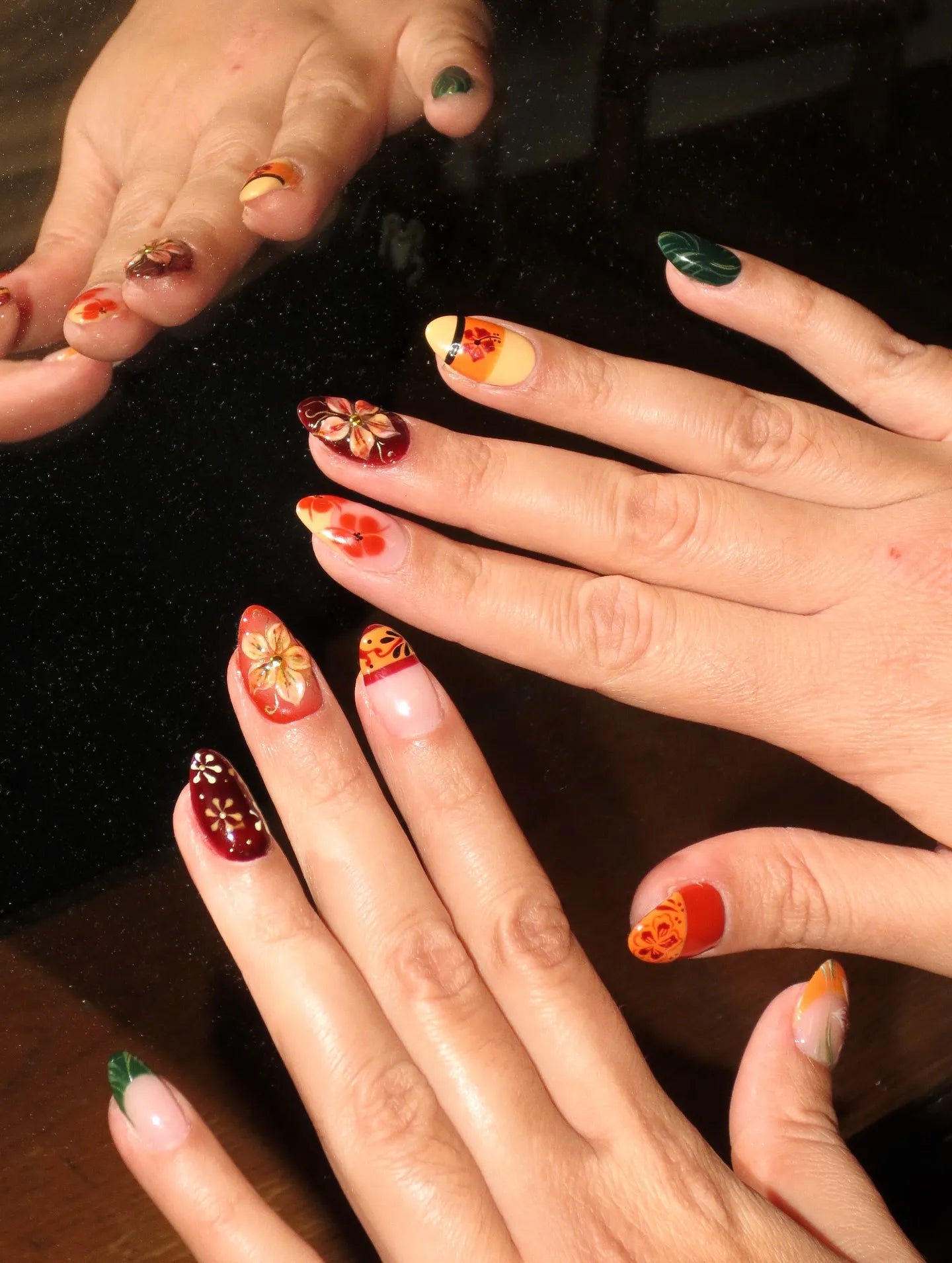 Hand with multicolor handmade press-on nails featuring tropical hibiscus and autumn floral designs.