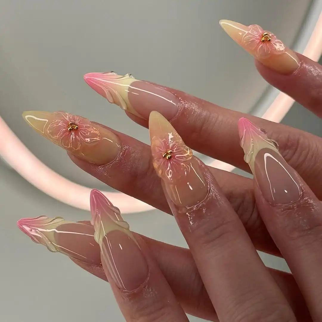 Hand with long almond-shaped press-on nails in pink and yellow with 3D floral design.