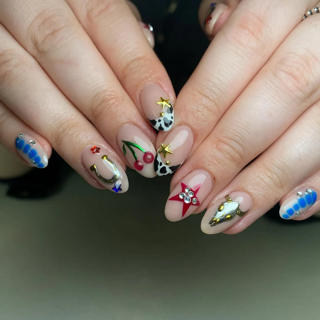Hand with handmade western cowgirl press-on nails featuring cow print, cherries, horseshoe, and star designs.