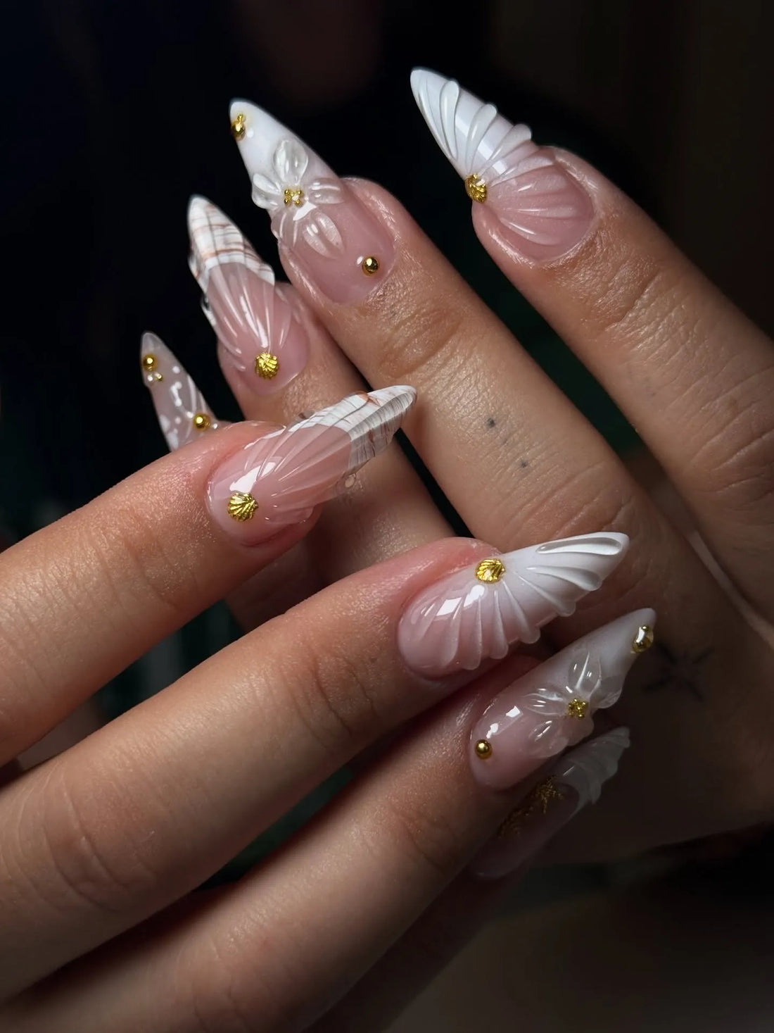 Handmade white 3D shell floral press-on nails with gold stud accents on natural hands