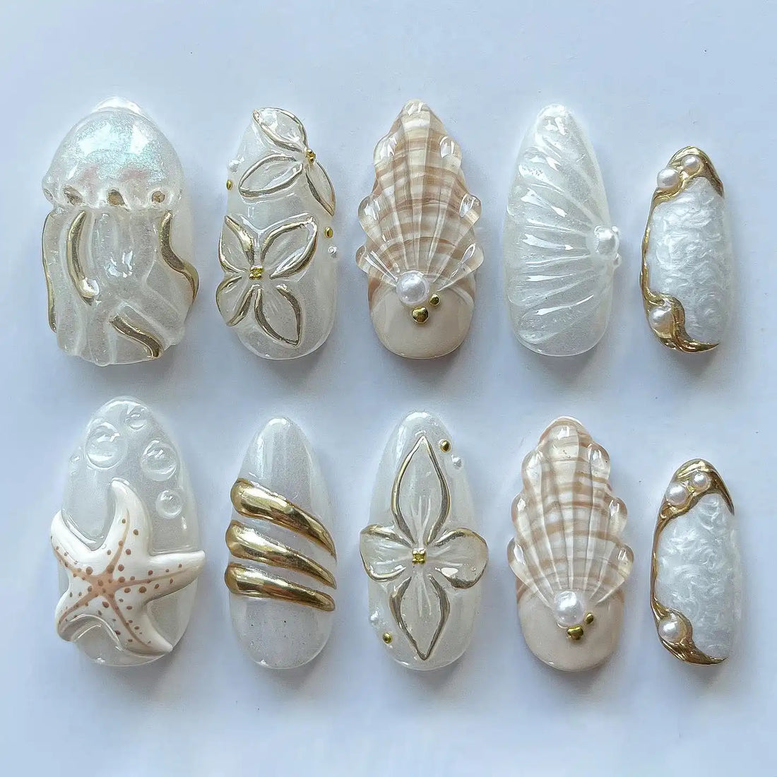Handmade white and gold ocean-themed press-on nails featuring seashell, starfish, and jellyfish designs.