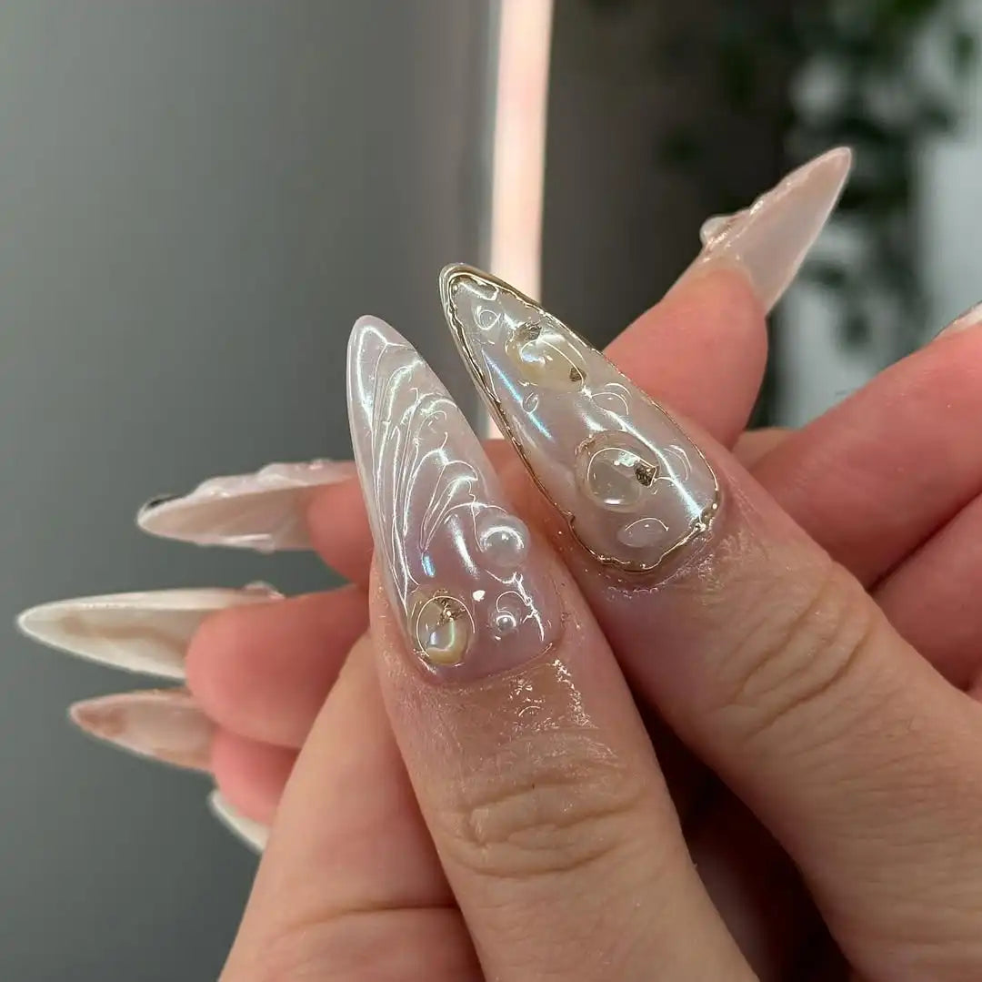 Hand with long handmade press-on nails, featuring white, pearl, and gold mermaid designs.