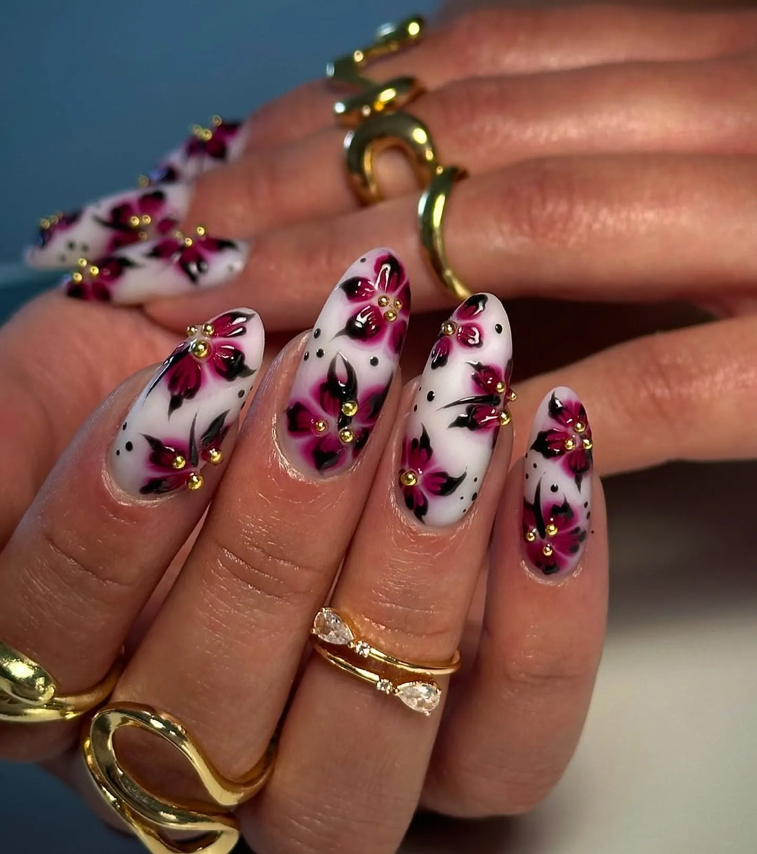 Hand with long white and pink floral press-on nails with gold accents and artistic dots