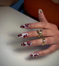 Hand with long white and pink floral press-on nails, gold dot accents, and gold rings