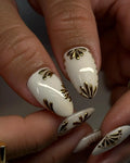 Handmade white press-on nails with gold floral accents, almond shape, close-up view